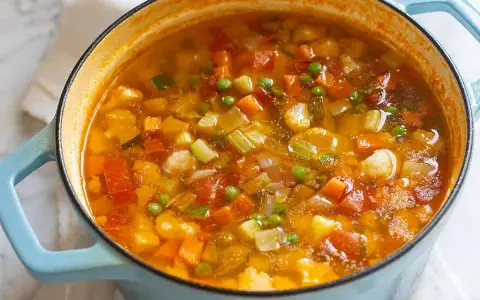 Un fumante minestrone di verdure in una pentola azzurra, ricco di carote, zucchine, piselli e cavolfiore.