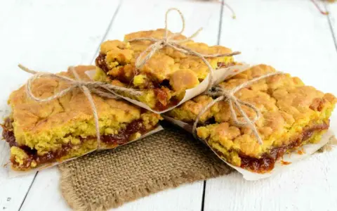 Tre deliziose fette di torta con marmellata, legate con spago e avvolte in carta da forno, pronte per essere gustate.