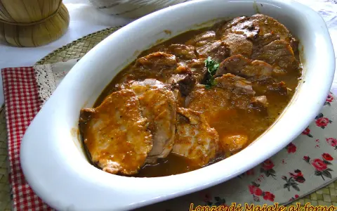 Arrosto di maiale morbido con sughetto, servito in una teglia bianca, pronto per essere gustato.