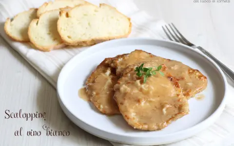 Tre scaloppine al vino bianco su un piatto bianco, guarnite con timo fresco, accompagnate da fette di pane tostato.