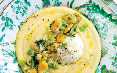 Un cremoso macco di fave fresche, guarnito con ricotta, fave intere, cipollotto e aneto, servito su un piatto decorato.