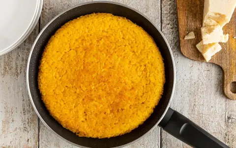 Un invitante riso al salto dorato in padella, pronto per essere gustato con scaglie di Parmigiano Reggiano.