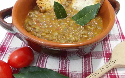 Un piatto fumante di lenticchie in umido, guarnito con crostini e foglie di alloro, pronto per essere gustato.