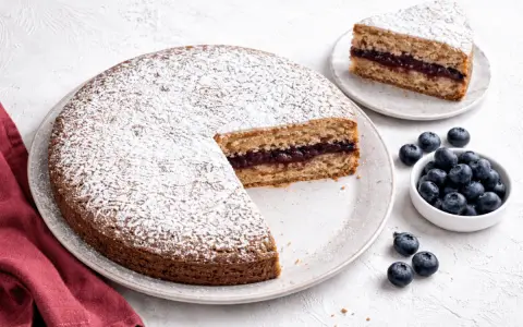 Torta senza glutine con marmellata di frutti di bosco, spolverata di zucchero a velo, accompagnata da mirtilli freschi.