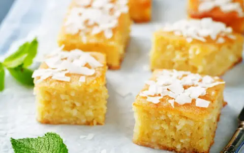 Deliziosi quadretti di torta al cocco, guarniti con scaglie di cocco e foglioline di menta fresca.