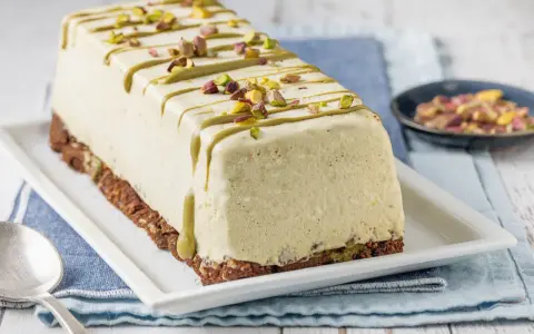Semifreddo al pistacchio, un dolce gelato decorato con glassa verde e granella di pistacchi, su una base croccante.