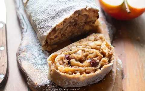 Delizioso strudel di mele con pasta sfoglia, cosparso di zucchero a velo, su un tagliere di legno.