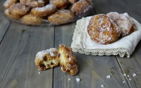 Frittelle di riso ricetta della nonna: dolcetti dorati e zuccherati, alcuni su un piatto, altri su un pizzo, uno aperto rivela l'interno morbido.