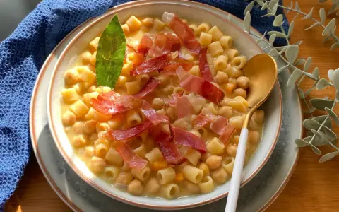 Un piatto fumante di pasta e ceci, arricchito da fette di prosciutto crudo e una foglia di alloro.