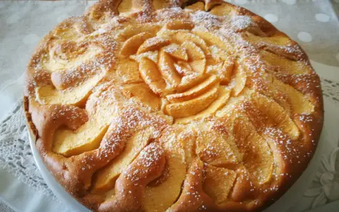 Una deliziosa torta di mele senza glutine, decorata con mele a forma di rosa e spolverata di zucchero a velo.