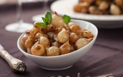 Ciotola di cipolle in agrodolce caramellate, guarnite con menta fresca.