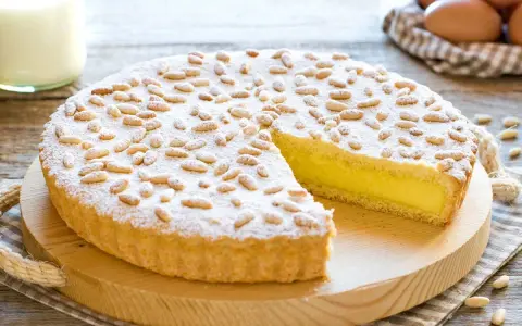 Una deliziosa torta della nonna, con crema gialla, ricoperta di pinoli e zucchero a velo, pronta per essere gustata.