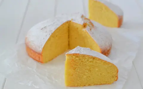 A fluffy lemon cake dusted with powdered sugar, with two slices cut out.