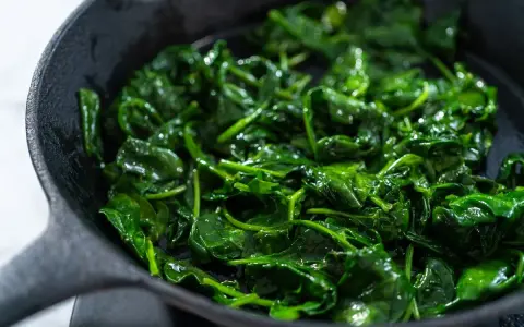 Spinaci freschi e lucidi che sfrigolano in una padella di ghisa, pronti per essere gustati.