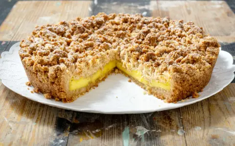 Sbriciolata alla crema con una crosta dorata e un ripieno giallo brillante, cosparsa di zucchero a velo.