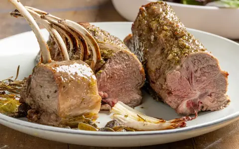 Costolette di agnello al forno succulente, condite con erbe aromatiche, servite su un piatto con verdure arrosto.