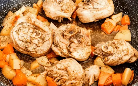 Porzioni di ossobuco di tacchino cotte in padella con patate e carote a cubetti, condite con erbe aromatiche.