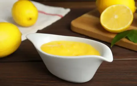 Una ciotola bianca contiene una vellutata crema al limone, con limoni freschi sullo sfondo.