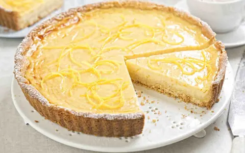 Una deliziosa crostata con crema pasticcera, guarnita con scorza di limone e spolverata di zucchero a velo.