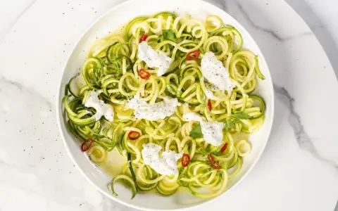 Spaghetti di zucchine freschi con ricotta cremosa, peperoncino e menta, un piatto leggero e colorato.