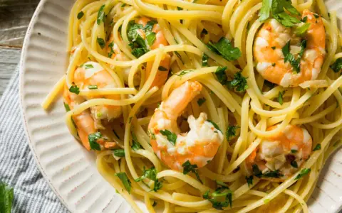 Un piatto invitante di pasta con gamberetti, condita con prezzemolo fresco e servita su un piatto bianco.
