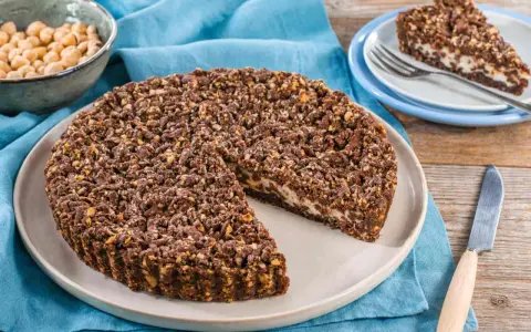 Sbriciolata ricotta e cioccolato con croccante copertura di nocciole. Una fetta è già servita su un piattino.