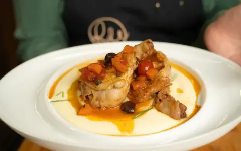 Pollo alla cacciatora ricetta della nonna: succulenti pezzi di pollo in umido con pomodoro, olive e carote, serviti su un letto di polenta cremosa.