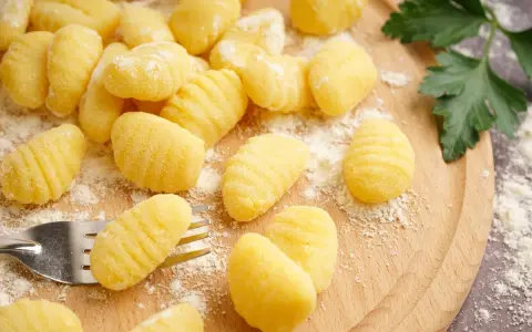 Gnocchi fatti in casa pronti per la friggitrice ad aria, spolverati di farina su un tagliere di legno.