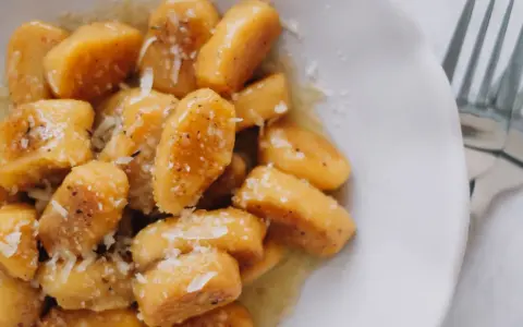 Gnocchi di zucca dorati, conditi con burro fuso, pepe nero e scaglie di parmigiano, pronti per essere gustati.
