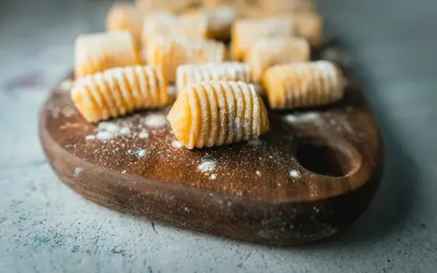 Gnocchi di patate fatti in casa, pronti per essere cucinati, spolverati di farina su un tagliere di legno.