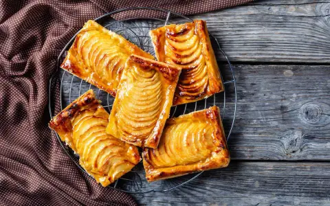 Deliziosi dolci con pasta sfoglia rettangolare, ripieni di mele caramellate, su una griglia di raffreddamento.