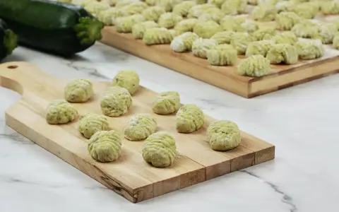 Gnocchi di zucchine freschi, pronti per essere cotti, disposti su taglieri di legno.