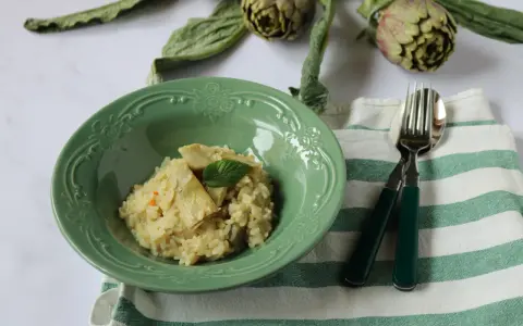 Un cremoso risotto con carciofi freschi, guarnito con una fogliolina di menta, pronto per essere gustato.