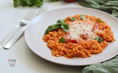 Un cremoso risotto al pomodoro, guarnito con basilico fresco e parmigiano grattugiato, pronto per essere gustato.