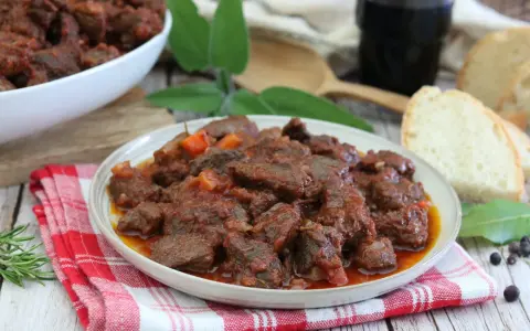 Cinghiale in umido fatto in casa da Benedetta, un piatto ricco e saporito, servito con pane fresco e un bicchiere di vino rosso.