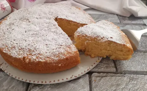 Una soffice torta al latte, spolverata di zucchero a velo, con una fetta appena tagliata pronta per essere gustata.