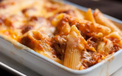 Un invitante piatto di pasta pasticciata al forno, con penne ricoperte da un ricco sugo e formaggio filante, pronto per essere gustato.