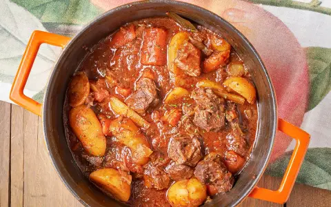 Un saporito spezzatino con patate, cotto lentamente in un tegame arancione, pronto per essere gustato.