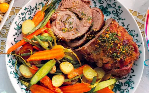 Un succulento agnello al forno, affettato e guarnito con erbe aromatiche, servito con patate novelle, carote e fagiolini.