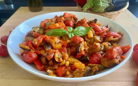 Caponata siciliana ricetta della nonna: melanzane, pomodori, peperoni e basilico in un piatto bianco.