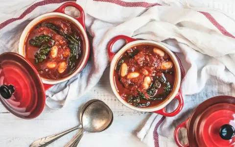 Due ciotole rosse con zuppa di cavolo nero e fagioli, pronte per essere gustate.