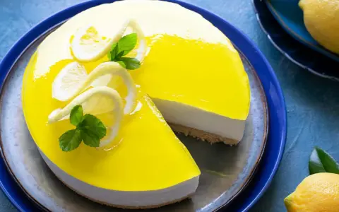 Delizioso cheesecake al limone con glassa gialla brillante, decorato con fette di limone e menta. Una fetta è stata tolta, rivelando la base croccante.