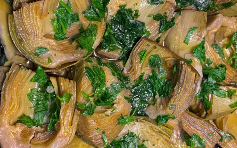 Deliziosi carciofi in padella, teneri e profumati, guarniti con prezzemolo fresco. Un piatto semplice e gustoso.