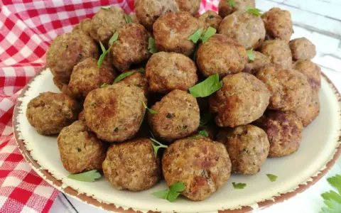 Un piatto colmo di polpette in bianco, dorate e profumate, guarnite con prezzemolo fresco.