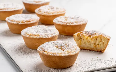 Deliziosi budini di riso in crostatina, spolverati di zucchero a velo. Uno è stato morso, rivelando il ripieno cremoso.