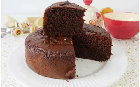 Una fetta di torta yogurt e cioccolato, soffice e golosa, è appoggiata su una torta intera. Sullo sfondo, una tazza rossa e un barattolo decorato.