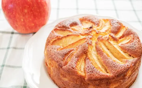 Torta di mele con yogurt, dorata e soffice, con mele a vista. Accanto, una mela rossa fresca.