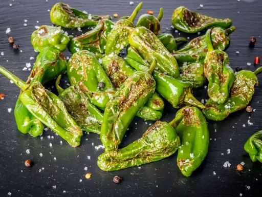 Friggitelli verdi, cotti in friggitrice ad aria, cosparsi di sale grosso e pepe nero su una superficie scura.