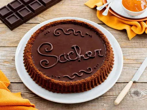 Una crostata morbida al cioccolato, decorata con la scritta "Sacher" in glassa, pronta per essere gustata.