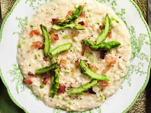 Un cremoso risotto asparagi e zafferano, guarnito con punte di asparagi freschi e cubetti croccanti di pancetta.